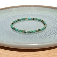 A boho beaded bracelet strung on transparent stretch cord using medium-sized Japanese miyuki glass beads in turquoise, dark teal and gold color