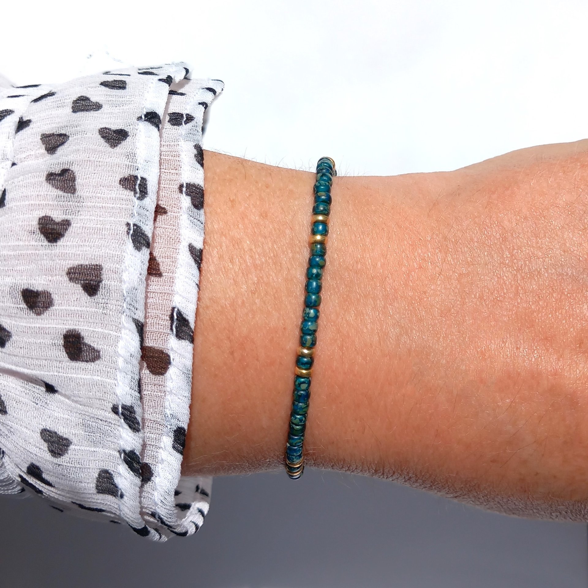 A boho beaded bracelet strung on transparent stretch cord using medium-sized Japanese miyuki glass beads in dark teal and gold color