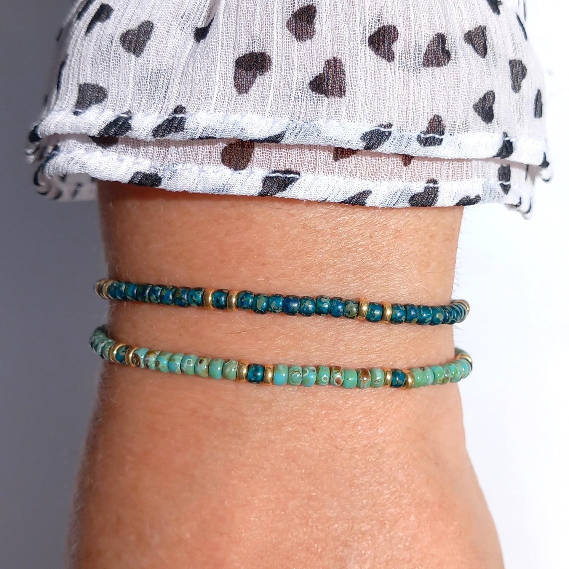 A boho beaded set of two bracelets strung on transparent stretch cord using medium-sized Japanese miyuki glass beads in turquoise, dark teal and gold color
