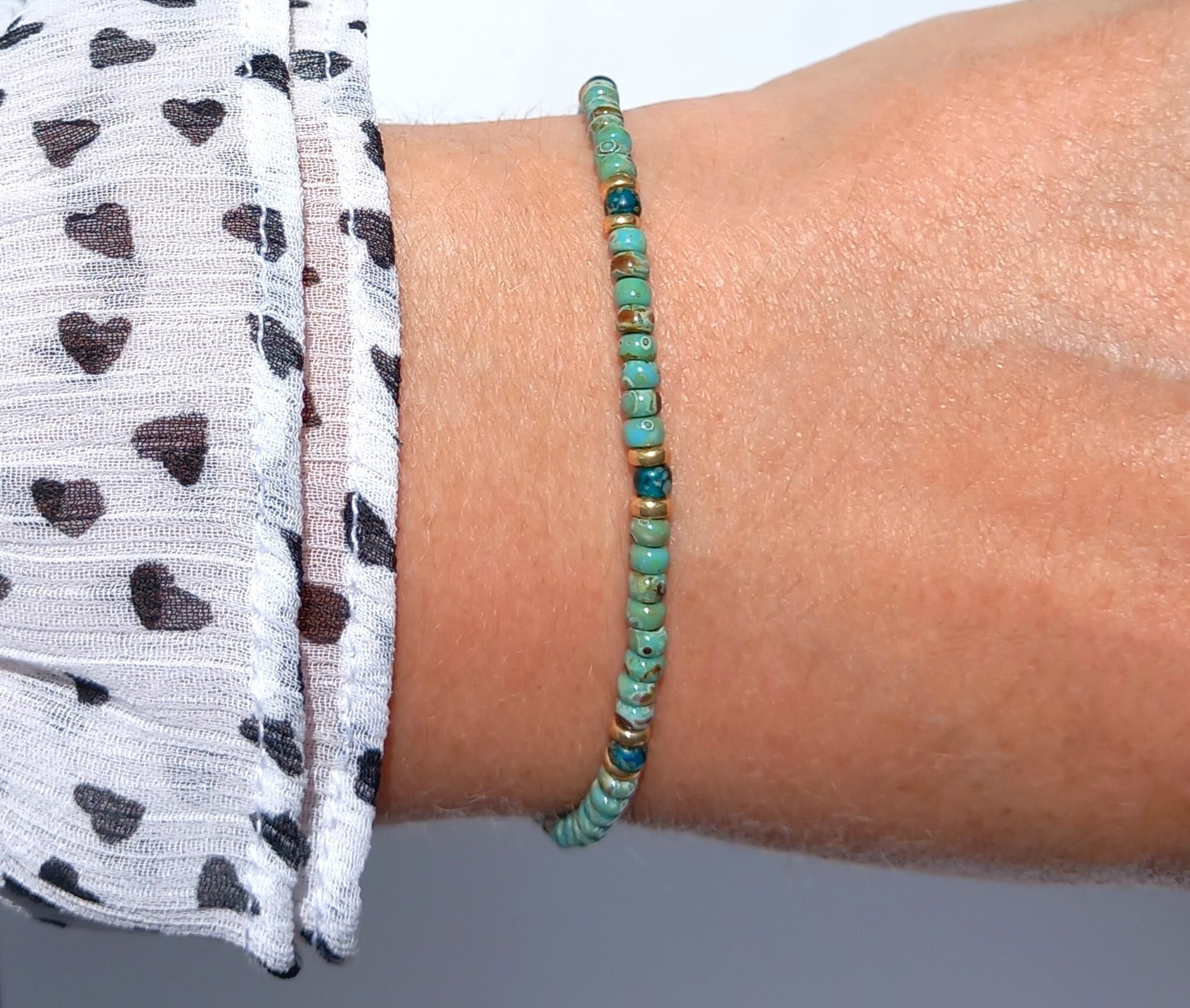 A boho beaded bracelet strung on transparent stretch cord using medium-sized Japanese miyuki glass beads in turquoise, dark teal and gold color