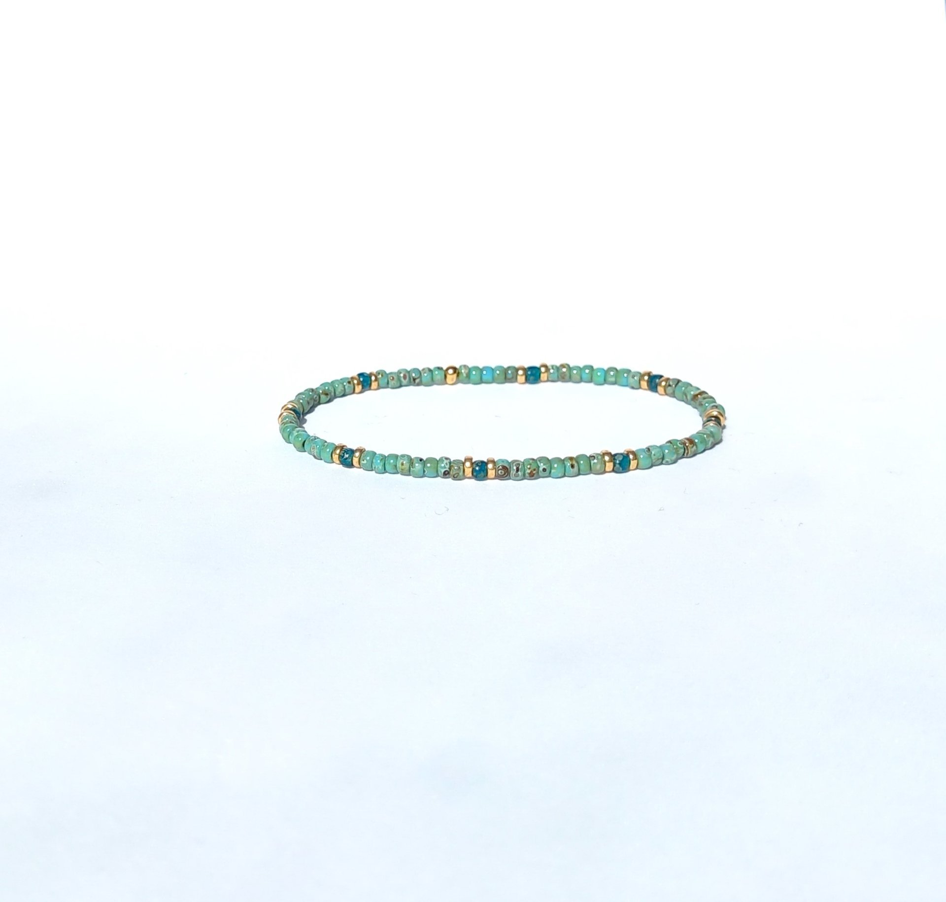 A boho beaded bracelet strung on transparent stretch cord using medium-sized Japanese miyuki glass beads in turquoise, dark teal and gold color