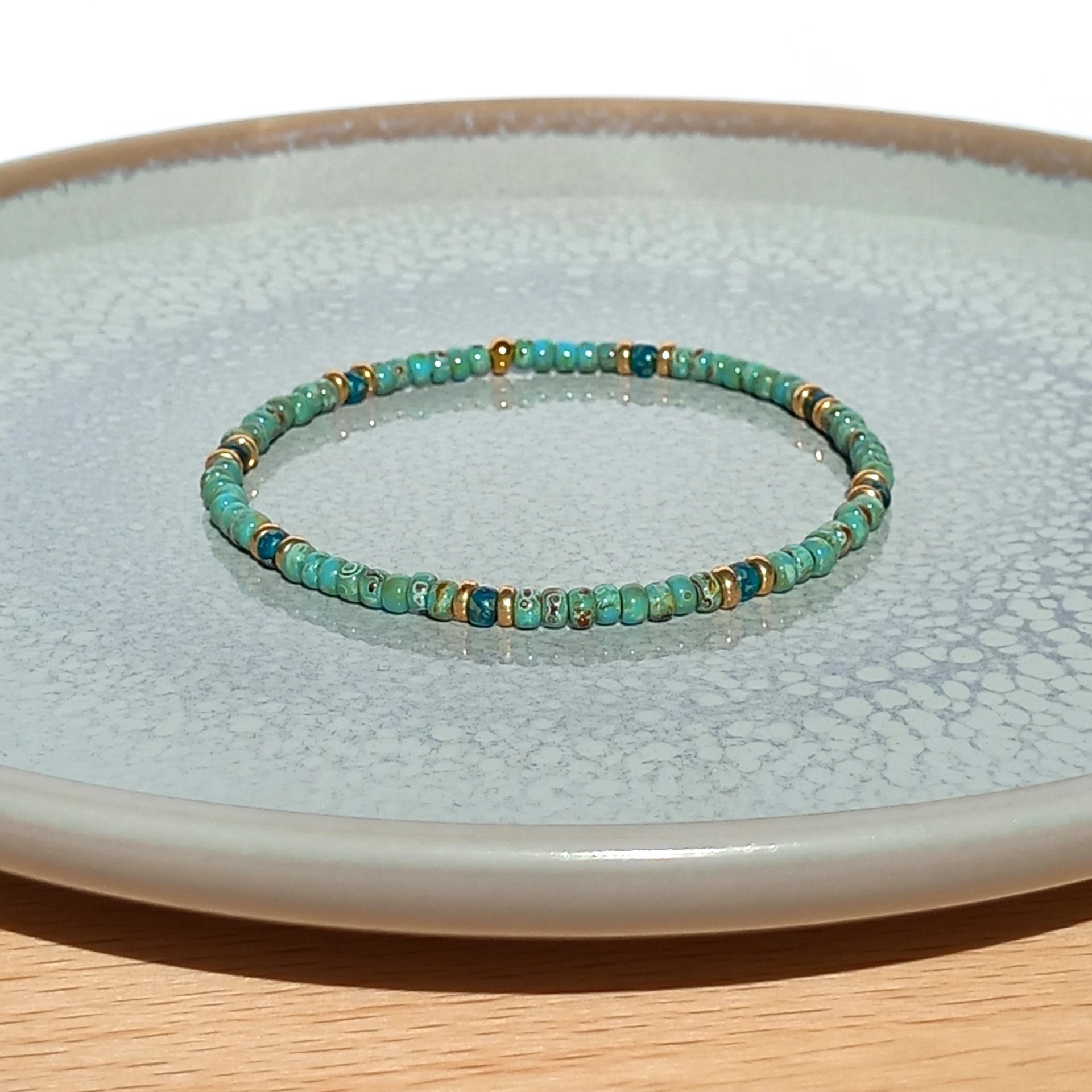 A boho beaded bracelet strung on transparent stretch cord using medium-sized Japanese miyuki glass beads in turquoise, dark teal and gold color