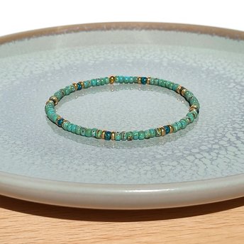 A boho beaded bracelet strung on transparent stretch cord using medium-sized Japanese miyuki glass beads in turquoise, dark teal and gold color